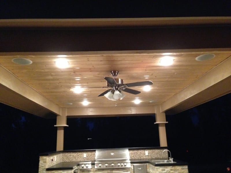 Covered stone outdoor kitchen: Tongue-and-groove knotty pine ceiling installation under roof canopy
